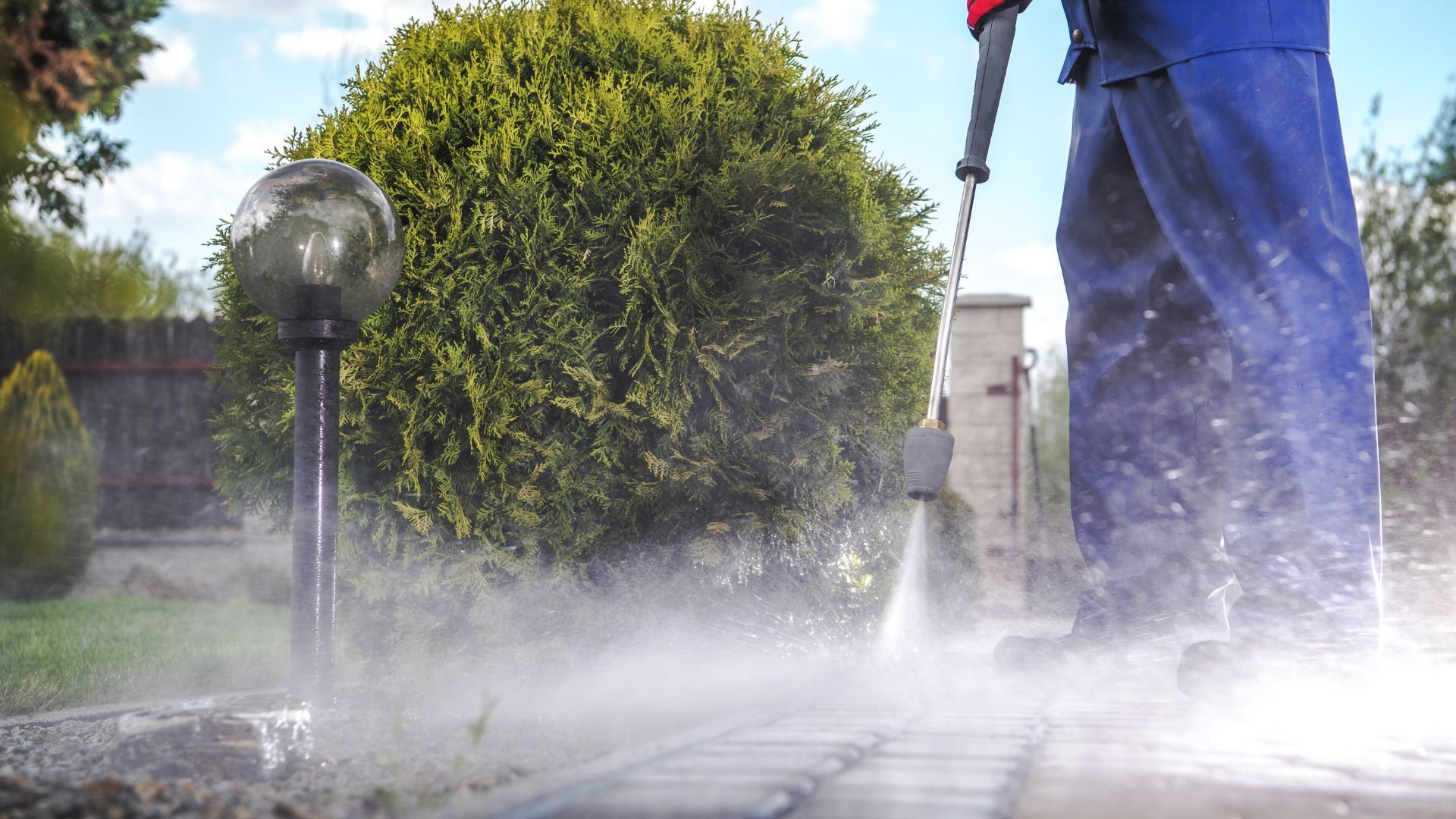 Power washing concrete near green bush and garden lamp