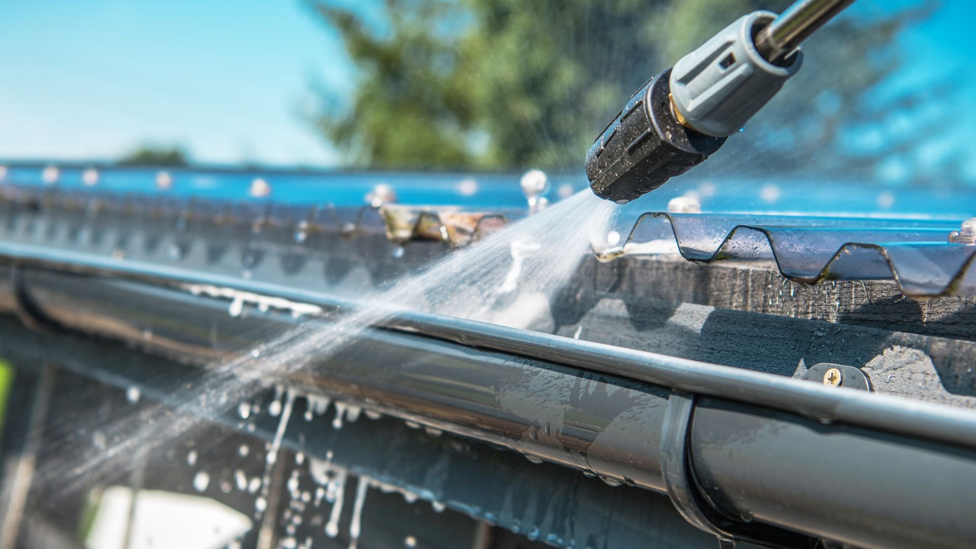 Power washer cleaning gutters with high-pressure water stream