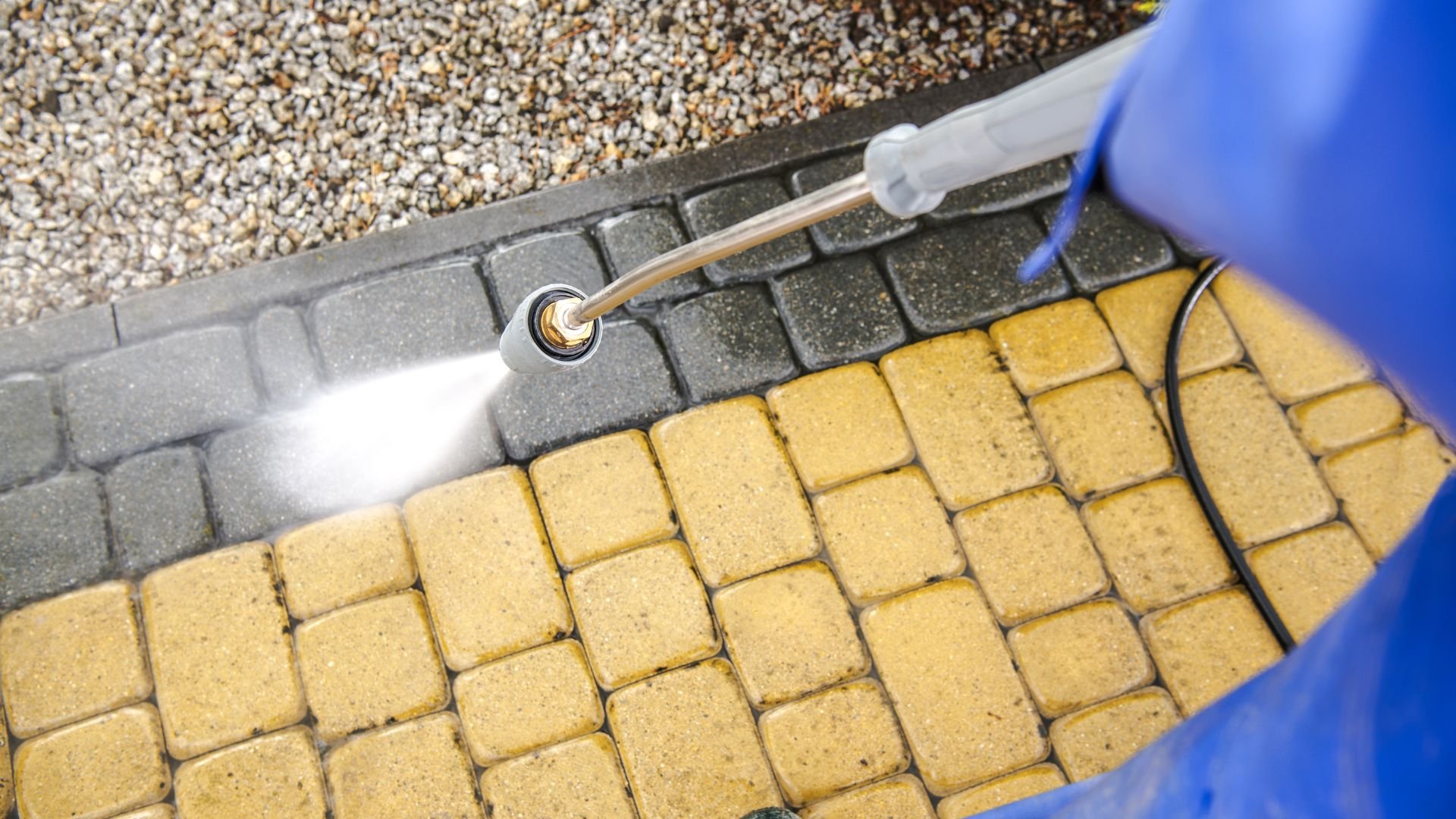 Pressure washer cleaning yellow and gray paving stones outdoors
