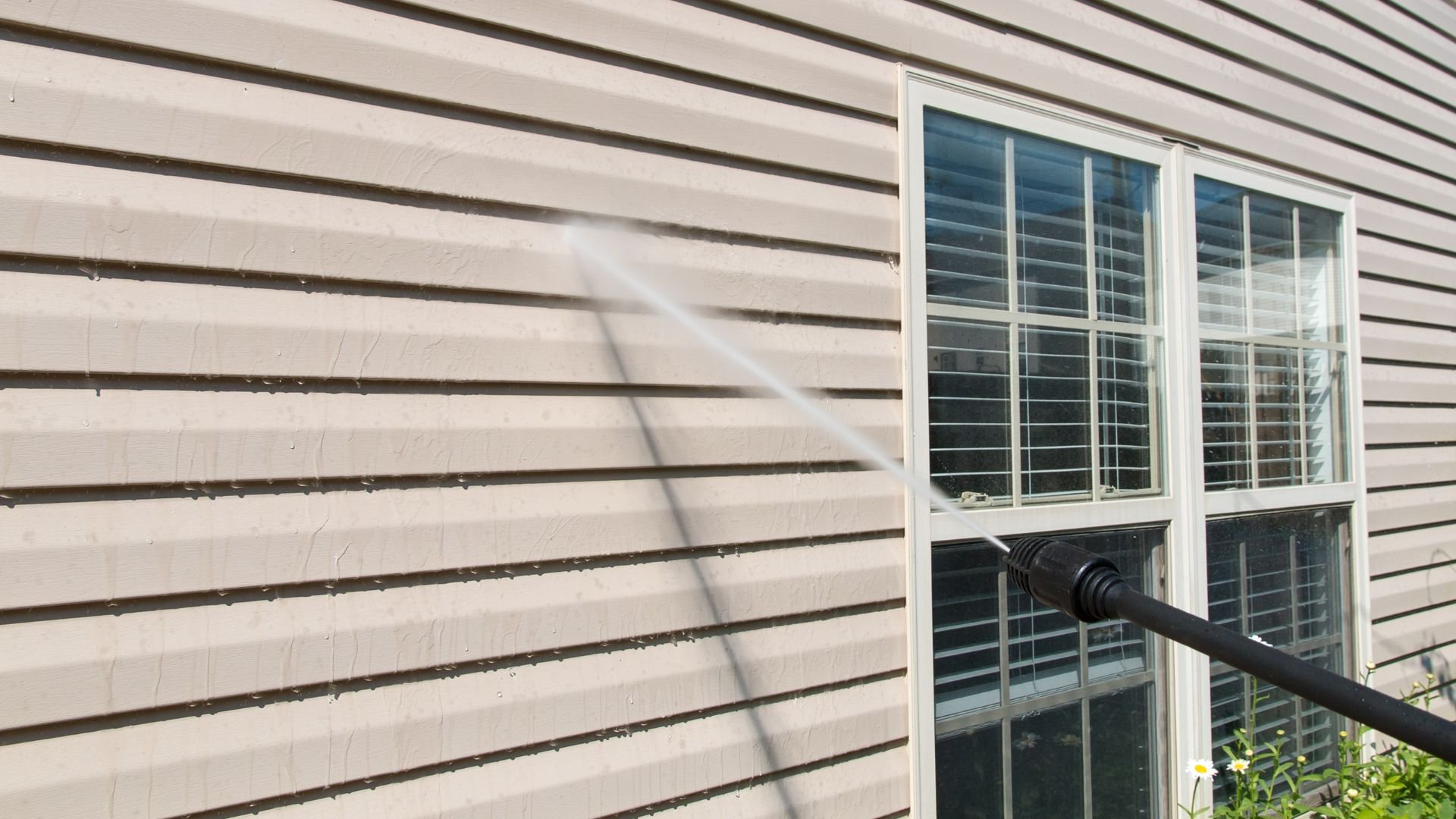 Power washer cleaning white siding and windows of a house